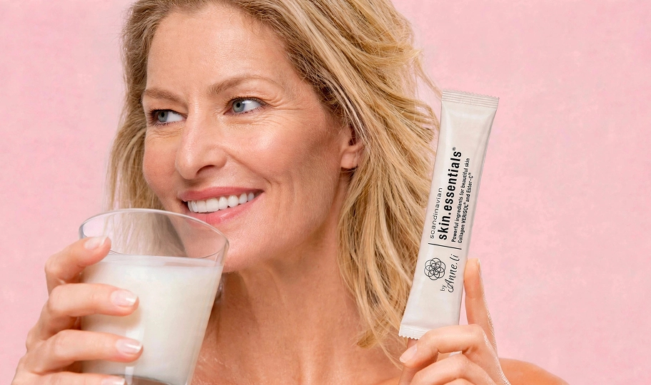 Natural Pharmaceuticals skin.essentials byAnne.li® Uśmiechnięta kobieta trzymająca szklankę oraz suplement diety skin.essentials byAnne.li®
